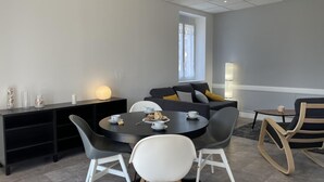 Ein moderner Essbereich mit einem runden Tisch, schwarz-weißen Stühlen, einem schwarzen Beistelltisch mit Dekoration und einem grauen Sofa mit Kissen.