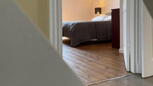 Ein Schlafzimmer mit Holzboden, einem Bett mit grauer Bettwäsche, einem Nachttisch und einer Wandlampe.