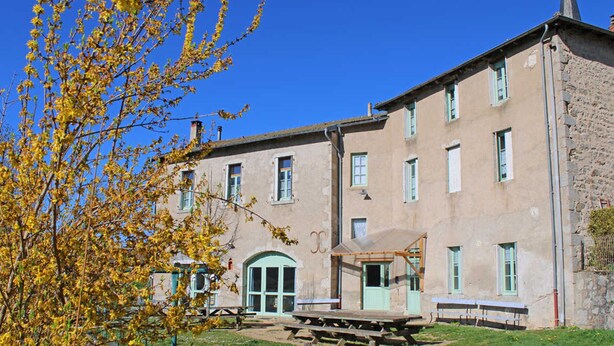 Un grand bâtiment doté de nombreuses fenêtres et d’une porte verte, entouré d’une zone herbeuse avec des tables de pique-nique.