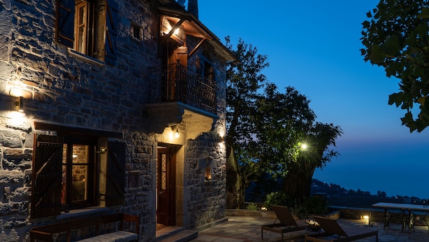 A stone building with a balcony, outdoor seating, and a view of the landscape.