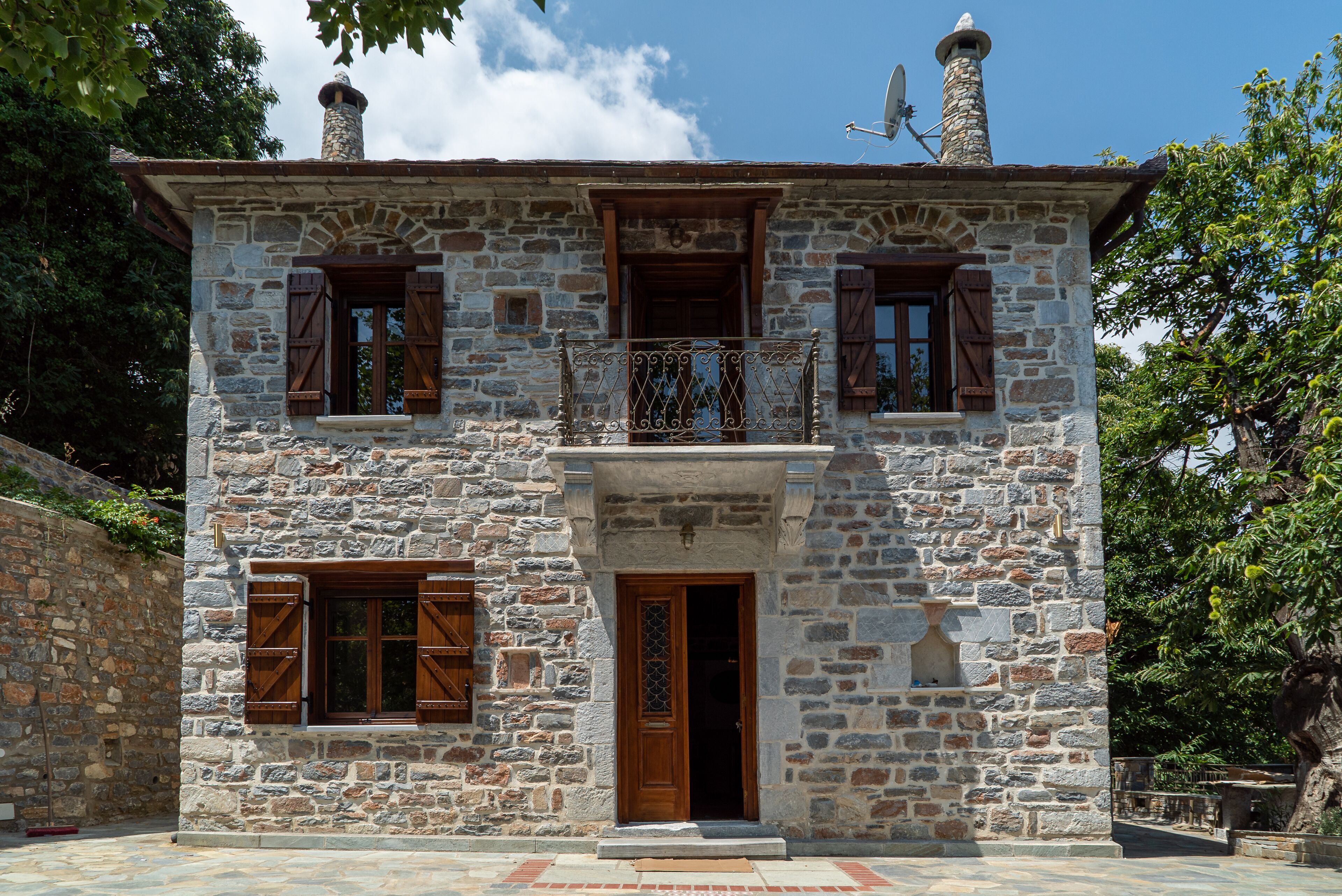 Un bâtiment en pierre avec une porte en bois, deux fenêtres avec volets et un balcon doté d’une balustrade en fer forgé.