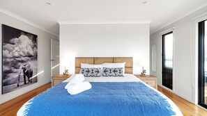 Une chambre moderne avec un grand lit, une tête de lit en bois et une vue sur la ville grâce à une grande fenêtre.