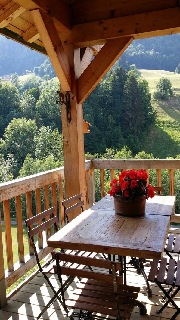 A wooden deck with a table and chairs, overlooking a green landscape. - La Chevrière, beautiful log cabin, panoramic views, near Megève (Flumet)