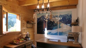 A wooden interior with a kitchen counter, a fruit bowl, a refrigerator, and a mountain view painting. - La Chevrière, beautiful log chalet, panoramic view, near Megève (Flumet)