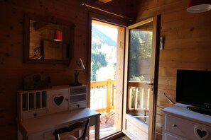 A wooden cabin room with a desk, chair, and a television on a dresser.