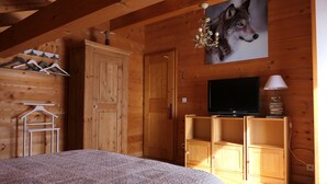 A wooden cabin bedroom with a bed, a TV, wooden cabinets, and a wall-mounted picture of a wolf. - La Chevrière, beautiful log chalet, panoramic view, near Megève (Flumet)