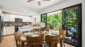Una cocina moderna con armarios blancos, un microondas y un comedor con una mesa lista para cuatro.