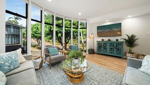 Un salón amplio con ventanas grandes, una mesa de centro redonda de cristal y un mueble aparador color turquesa.
