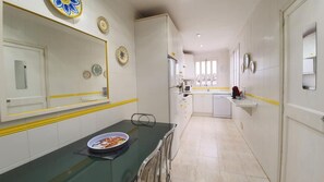Een smalle keuken met witte kastjes, een magnetron en een vaatwasser. Er hangen decoratieve borden aan de muur en een schaal met eten staat op het aanrecht.