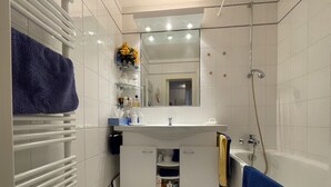Ein modernes Badezimmer mit weißen Fliesen, einem weißen Waschbecken, einem Spiegel über dem Waschbecken, einer Duschkabine und einem Handtuchhalter mit blauen Handtüchern.