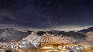 Eine Berglandschaft bei Nacht, mit einer Stadt, die im Tal darunter beleuchtet ist.
