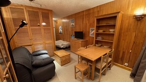 Ein gemütlicher, kompakter Wohnraum mit einer Couch, einem Esstisch mit Stühlen, einem Fernseher und Holzregalen.