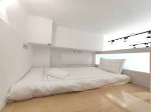 A minimalist bedroom with a single bed, a headboard, and a window with a light fixture above it. - Tokyo Loft duplex apt (Taipei)