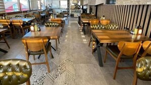 A modern restaurant interior with long wooden tables and leather chairs, a patterned rug, and a stone accent wall. - Yalova Sezon Hotel (Yalova)