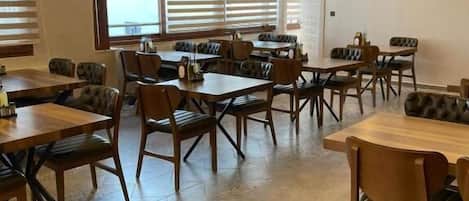 A restaurant with multiple tables and chairs, large windows with blinds, and a modern ceiling design.