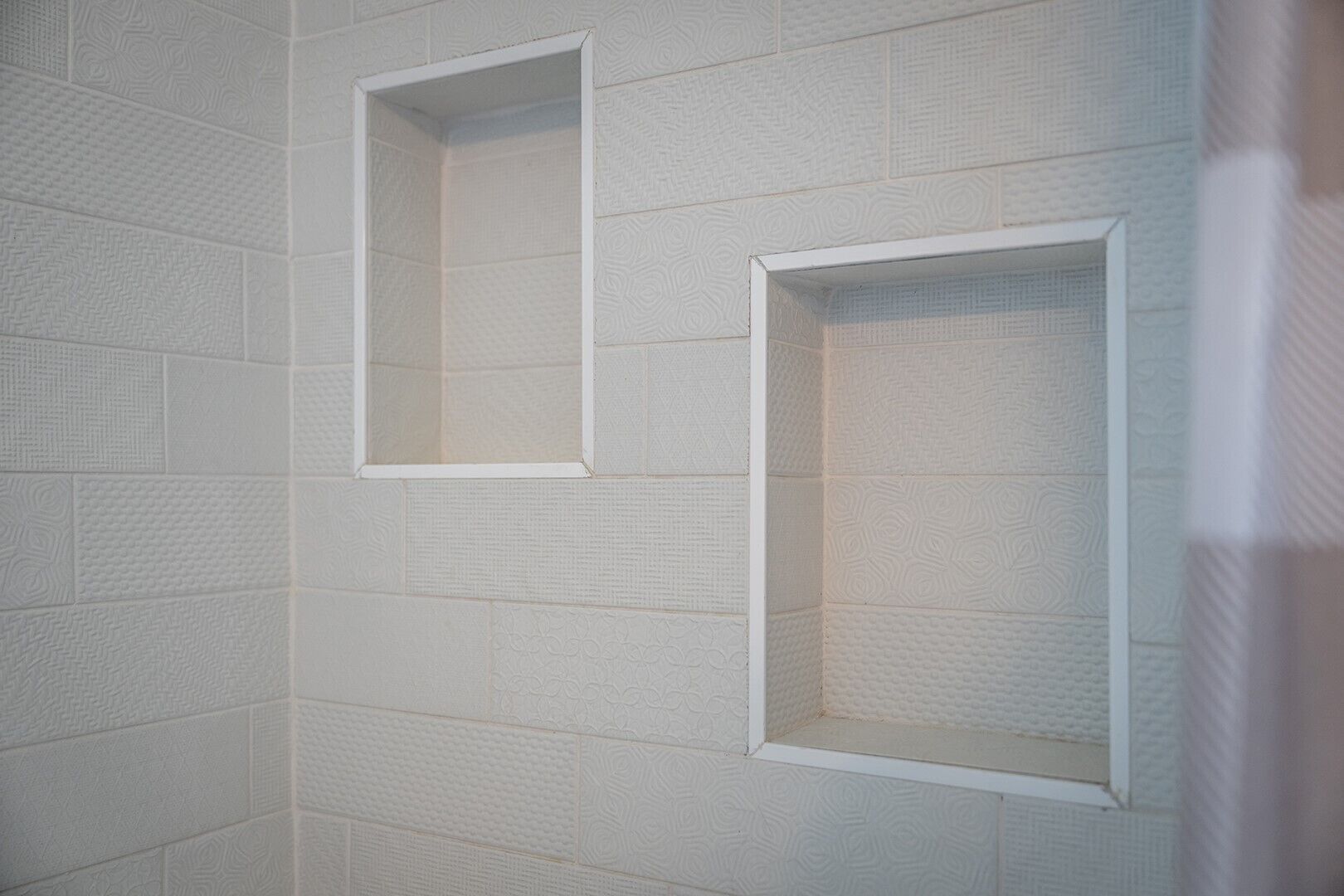 A bathroom with textured white tiles and two empty framed spaces on the wall.