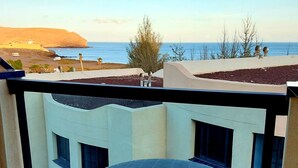 Un balcone con un tavolo rotondo e due sedie, con vista su una zona costiera, edifici e il mare.