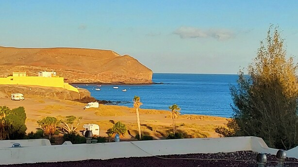 Paesaggio costiero con vista chiara sul mare, un edificio giallo e una struttura bianca sulla spiaggia.