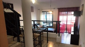 Una scala conduce a una zona pranzo con tavolo e sedie, una finestra con tende e un televisore su un mobile.
