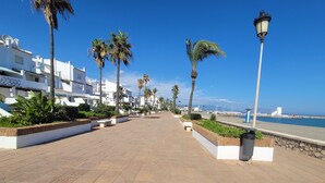 A paved walkway lined with palm trees and benches, leading to a beach with boats and a lighthouse. - Modern Apartment With Pool Close to Estepona, ES (Manilva)