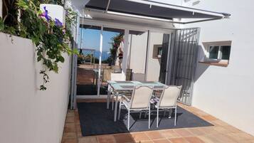 Eine Terrasse im Freien mit Tisch und Stühlen, eine überdachte Sitzecke und Blick aufs Meer.