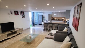 A modern living room with a sofa, coffee table, and TV. There is a kitchen area with bar stools and a dining table. - Modern Apartment With Pool Close to Estepona, ES (Manilva)