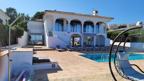 A pool area with lounge chairs, a stone-tiled deck, and a building with a white facade and arches. - Modern Apartment With Pool Close to Estepona, ES (Manilva)