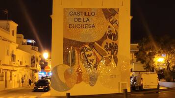 Ein belebter Straßenabend mit einer großen Werbetafel, auf der 'CASTILLO DE LA DUQUESSA' aus dem Jahr 2012 beworben wird.