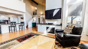 A modern living room with a fireplace, a black leather sofa, and a flat-screen TV mounted on the wall.