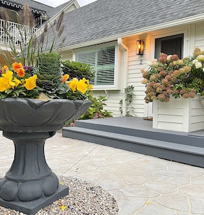 A house with a stone planter filled with yellow flowers, a grey roof, and a white exterior wall.
