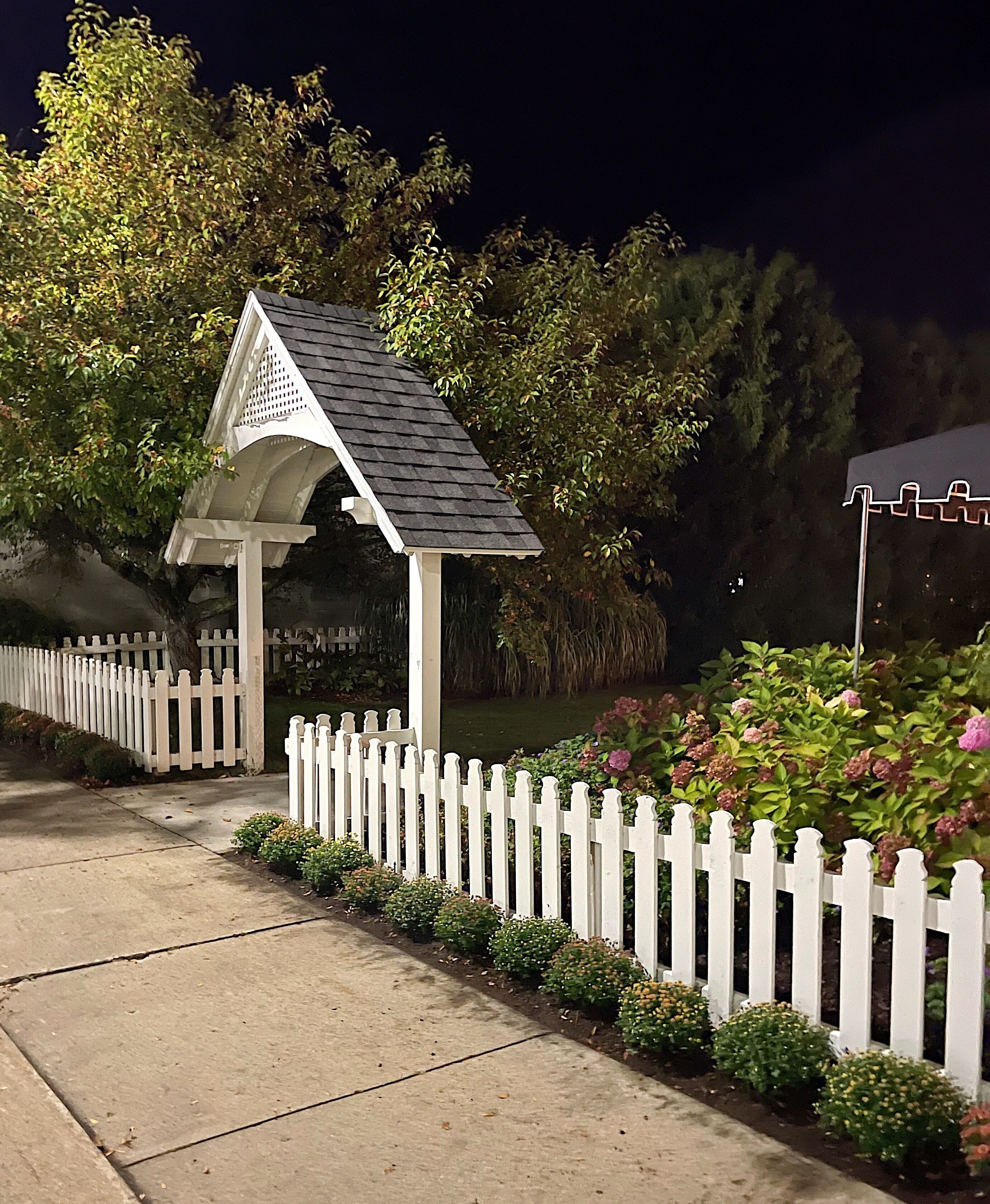 A gazebo with a white picket fence and a pond in the background.