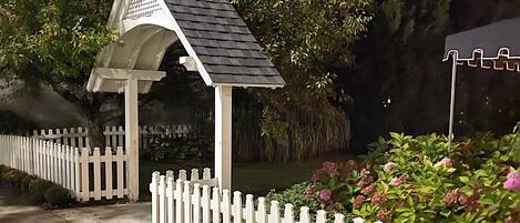 A gazebo with a white picket fence and a pond in the background.