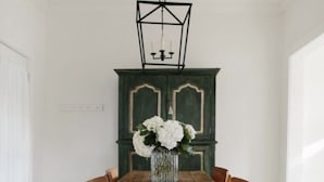 Une salle à manger avec une table en bois, six chaises, un vase de fleurs et un buffet vert.