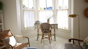 Une pièce comprenant un bureau, deux fauteuils en osier, une lampe et une vue sur une tour, visible à travers de grandes fenêtres.