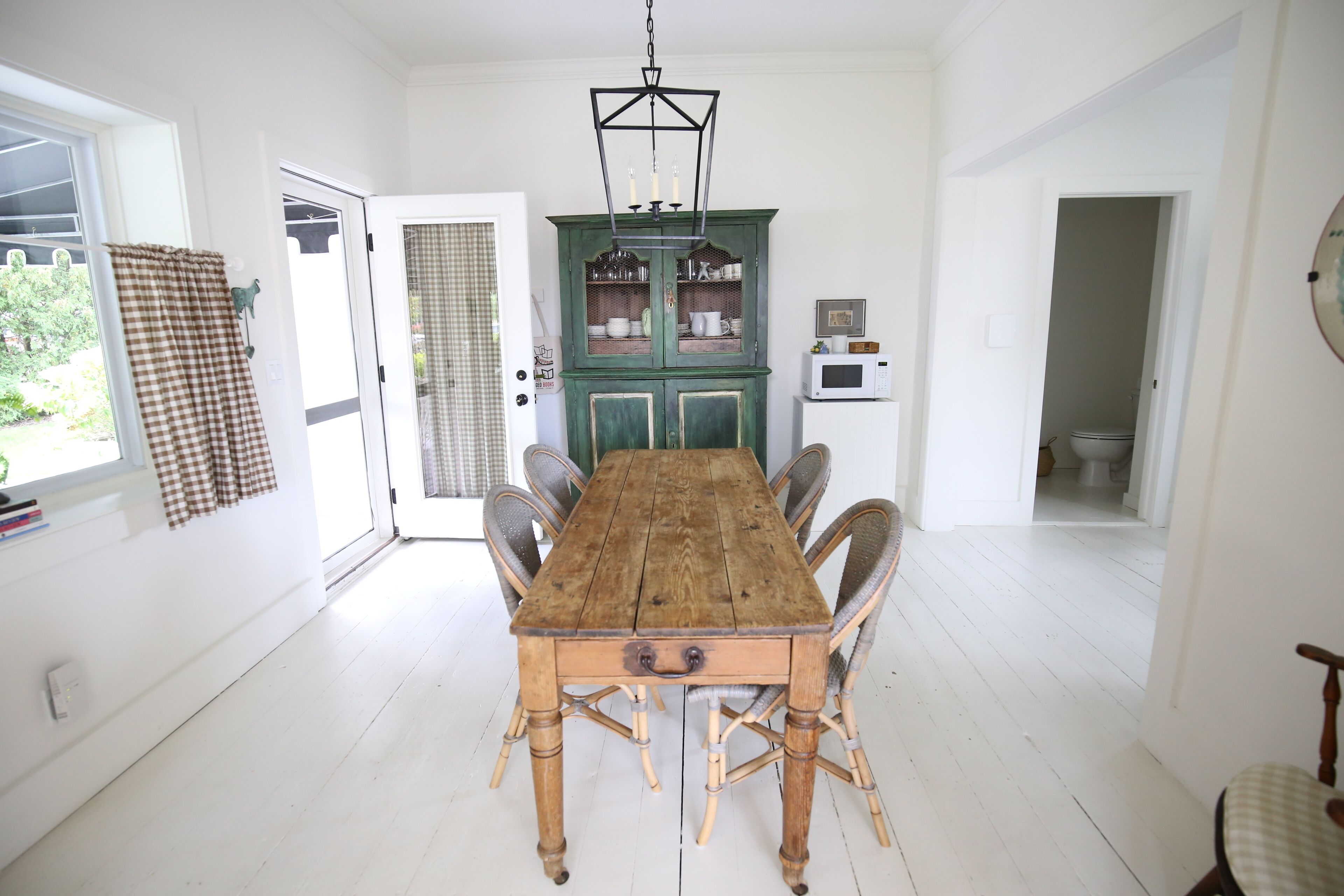 A dining room with a wooden table and chairs, a green cabinet with glass doors, and a white microwave on a shelf.
