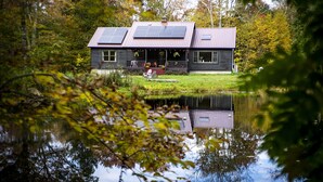 A house with solar panels, a dock, and a pond.