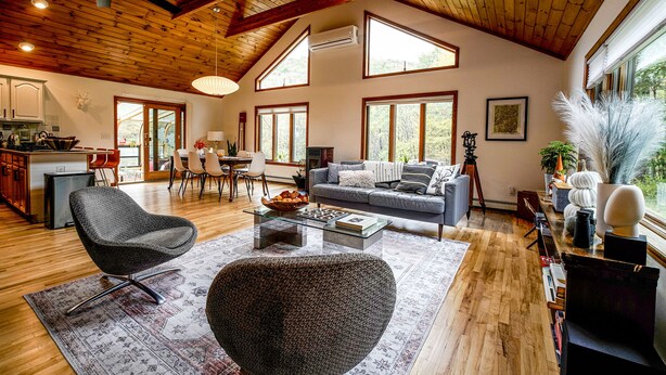 A spacious living area with a wooden ceiling, large windows, a grey sofa, and a modern coffee table.