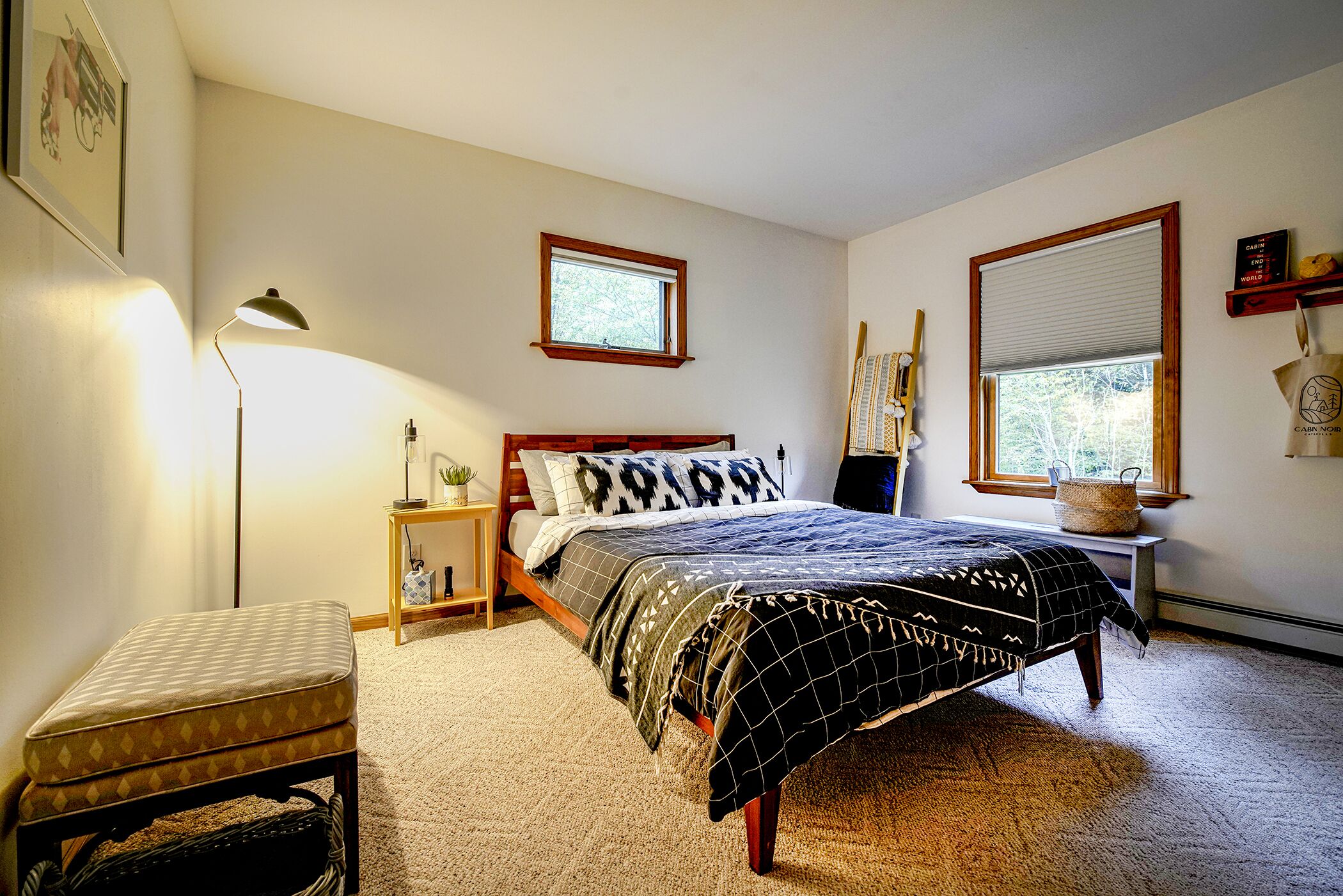 Un dormitorio con cama, mesitas de noche, una lámpara, una ventana y un pequeño banco.