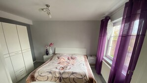 A bedroom with a bed, a nightstand, a wardrobe, and a window with curtains. - Vacation apartment Höhlenblick in Balve/Sauerland (Balve)
