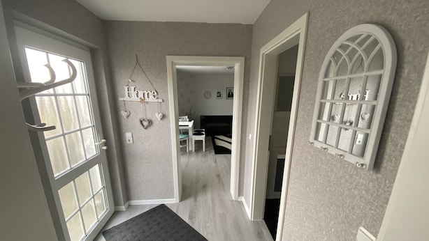 A hallway with a dark rug, a 'Home' sign, and a decorative window with heart-shaped cutouts. - Vacation apartment Höhlenblick in Balve/Sauerland (Balve)
