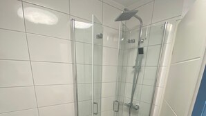 A modern bathroom with a glass-enclosed shower, white tiled walls, and a black marble floor. - Vacation apartment Höhlenblick in Balve/Sauerland (Balve)