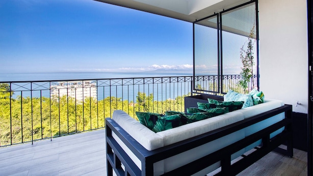A balcony with a white sofa and green cushions, overlooking a scenic view of the ocean and greenery. - Ocean-view terrace, Pool & BBQ, Conchas Chinas (Puerto Vallarta)