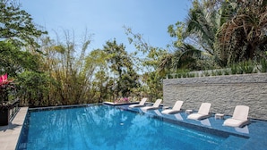 A rectangular swimming pool with clear blue water, surrounded by lush greenery and a stone wall. - Ocean-view terrace, Pool & BBQ, Conchas Chinas (Puerto Vallarta)