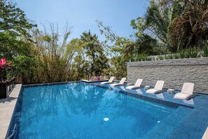 A rectangular swimming pool with clear blue water, surrounded by lush greenery and a stone wall. - Ocean-view terrace, Pool & BBQ, Conchas Chinas (Puerto Vallarta)