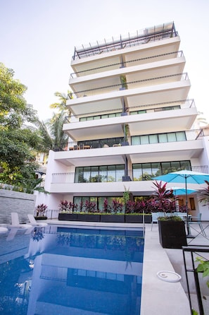 A multi-story hotel with a swimming pool, outdoor seating, and balconies.