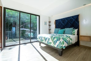 A bedroom with a bed, a nightstand, a window with a view of greenery, and a sliding glass door to a balcony. - Ocean-view terrace, Pool & BBQ, Conchas Chinas (Puerto Vallarta)