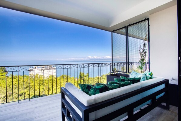 A balcony with a bed, a view of the sea, and a cityscape in the background.