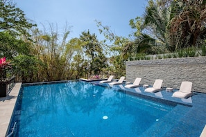 An outdoor swimming pool with clear blue water, surrounded by lush greenery and a stone wall. - Ocean-view terrace, Pool & BBQ, Conchas Chinas (Puerto Vallarta)