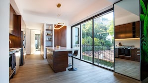 A modern kitchen with a central island, wooden flooring, and large sliding glass doors leading to a balcony. - Ocean-view terrace, Pool & BBQ, Conchas Chinas (Puerto Vallarta)