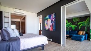 A modern bedroom with a large bed, a colorful abstract painting, and a blue sofa in the living area. - Ocean-view terrace, Pool & BBQ, Conchas Chinas (Puerto Vallarta)